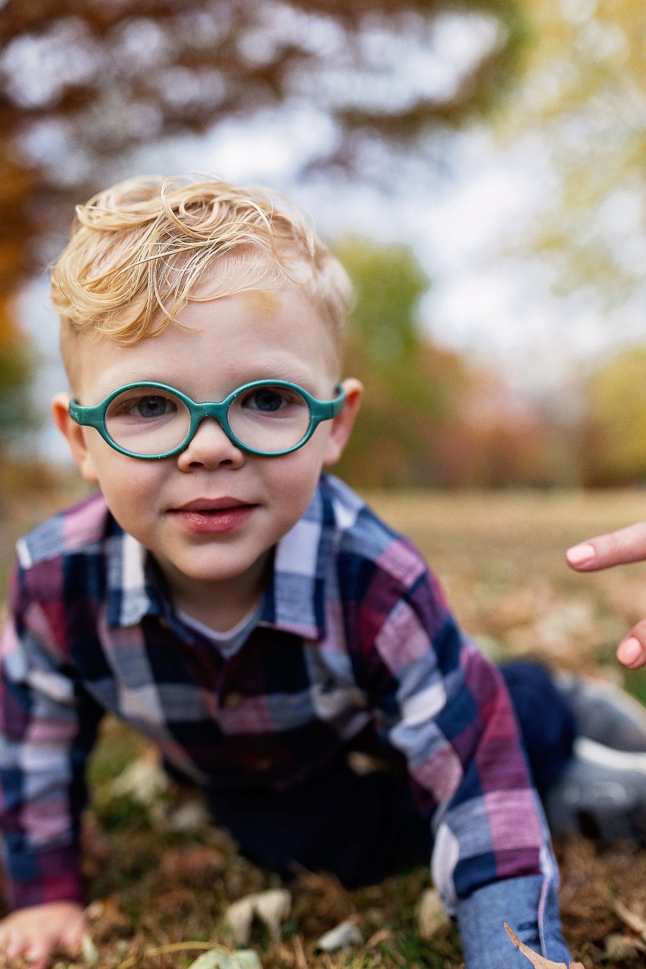 Toddler in green glasses crawling through autumn leaves