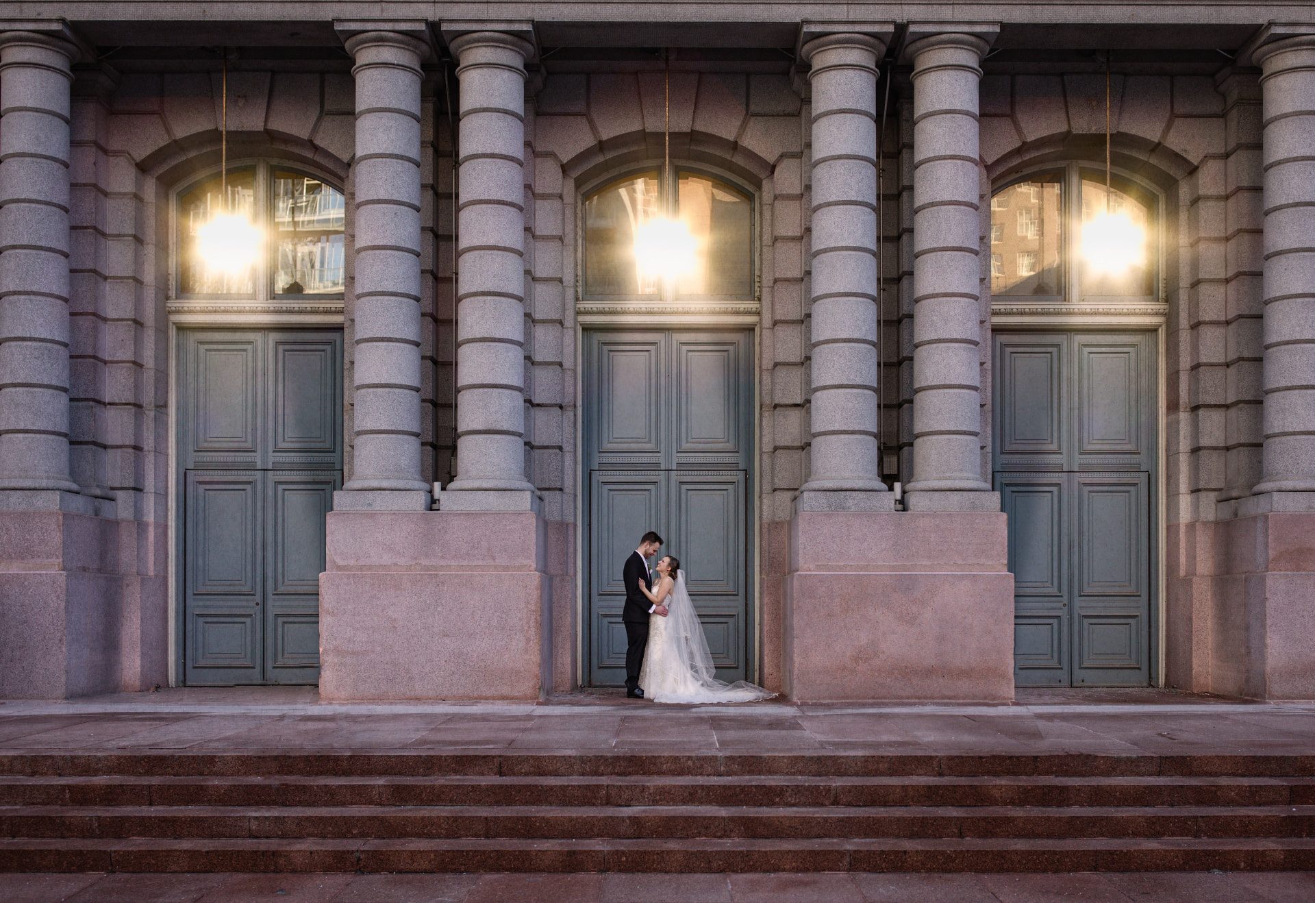 Bride and groom beneath sunlit stone columns on their wedding day