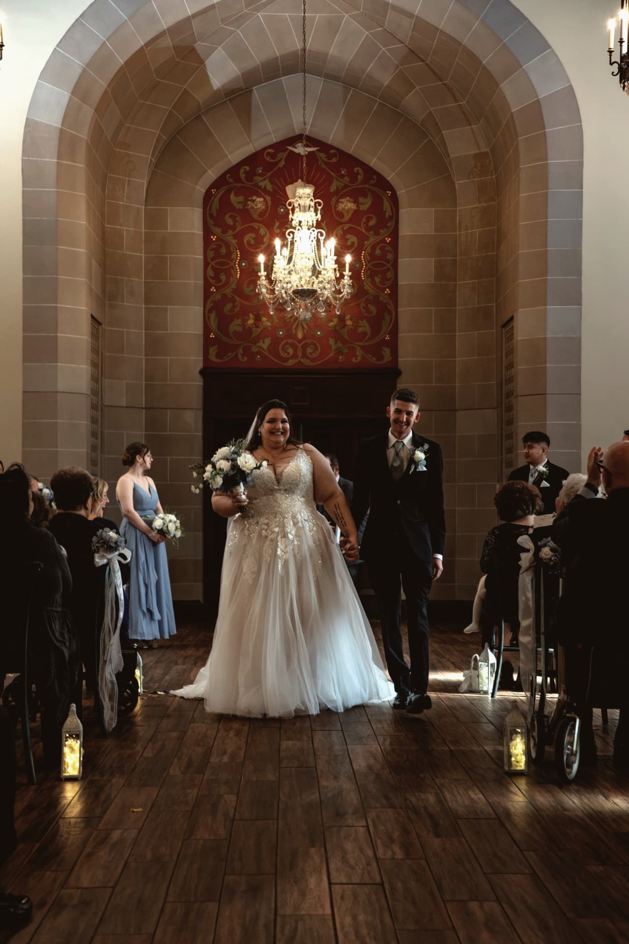 Newlyweds walking back up the aisle of a candlelit stone chapel