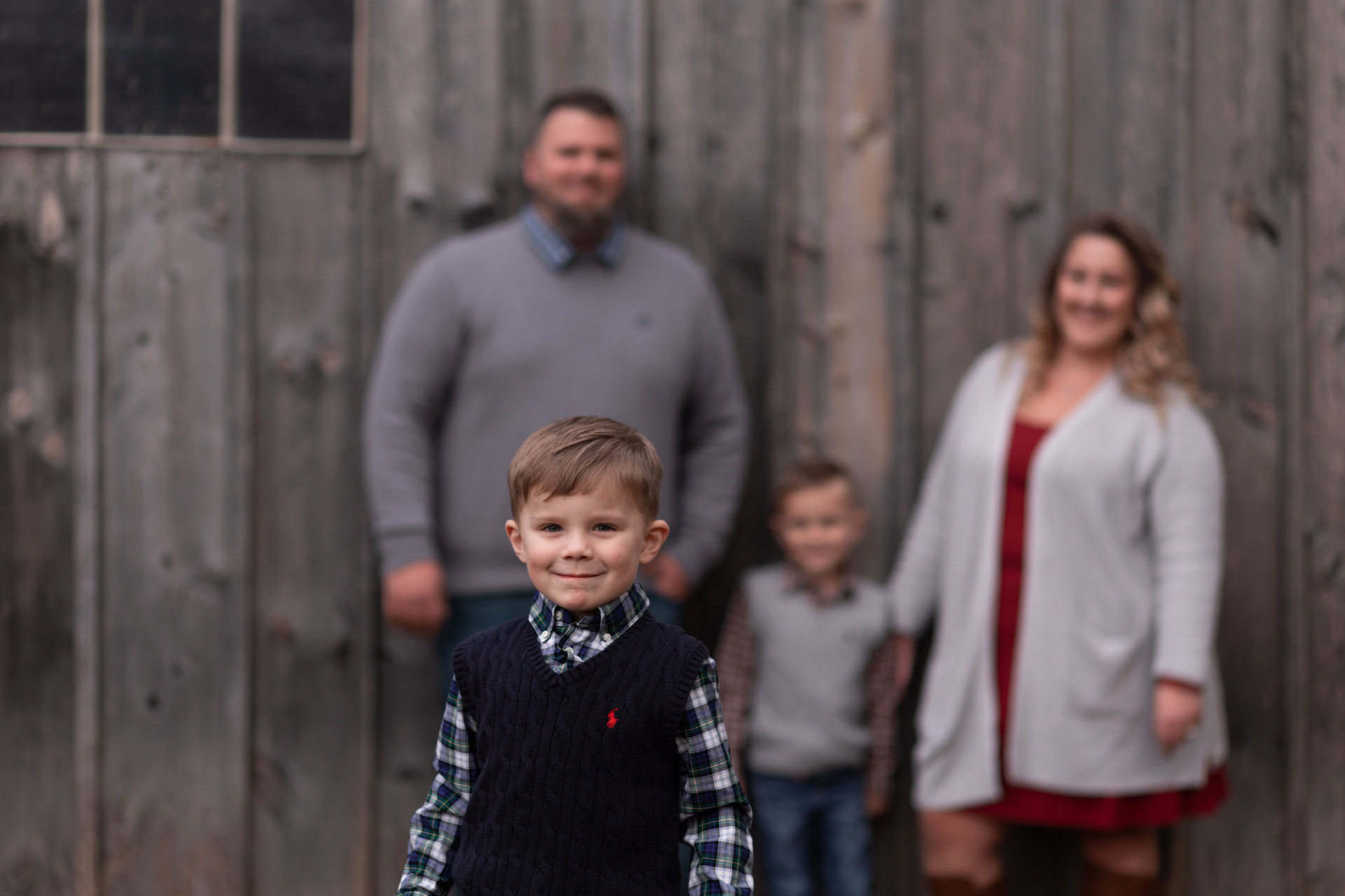 Young boy smiling in front of his family outside a weathered barn