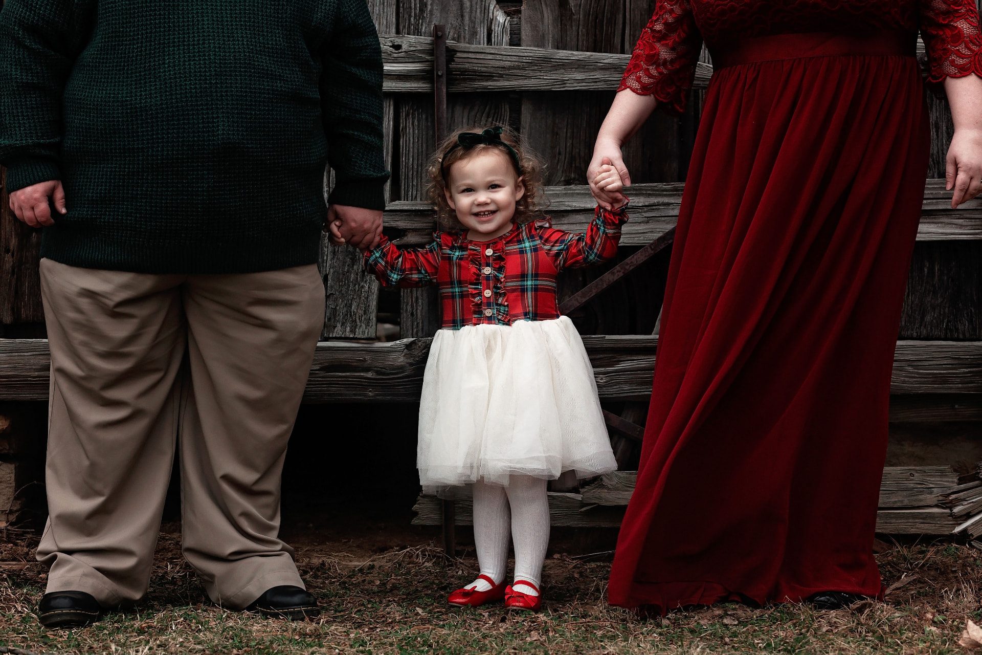 Little girl holding her parents’ hands during a Christmas family session