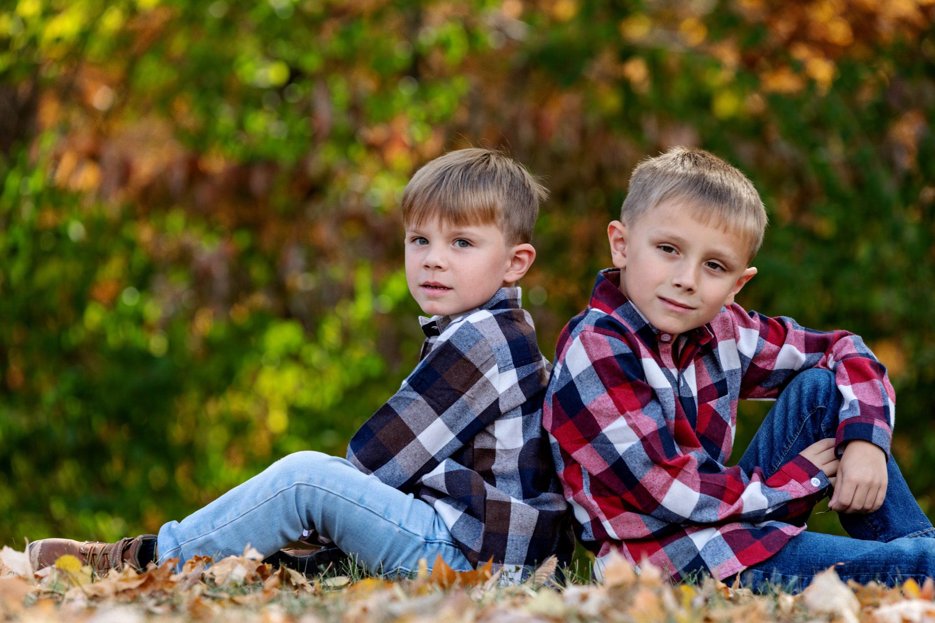 Two brothers sitting back to back among autumn leaves