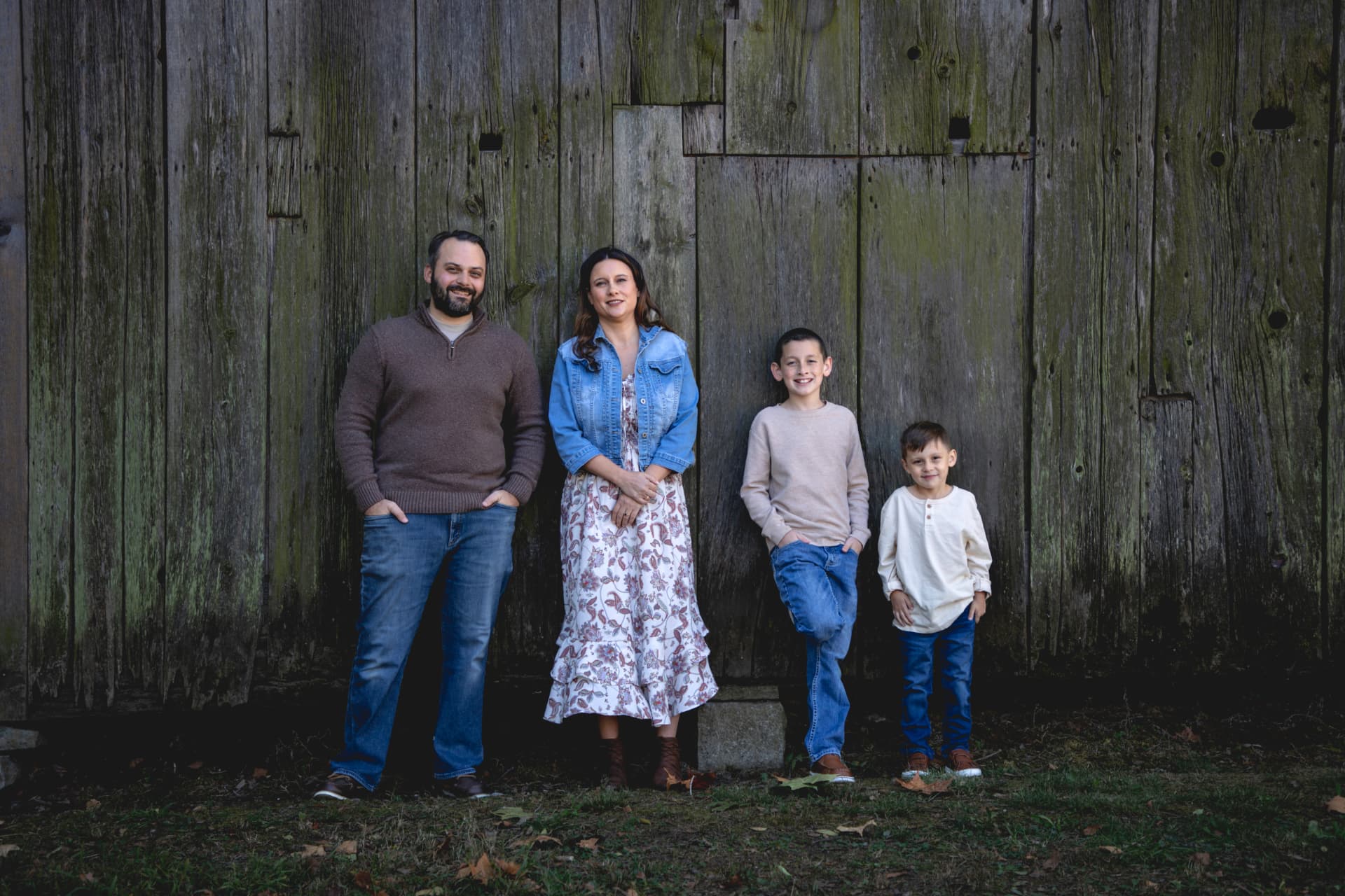 Family of four standing together in front of a weathered wooden barn