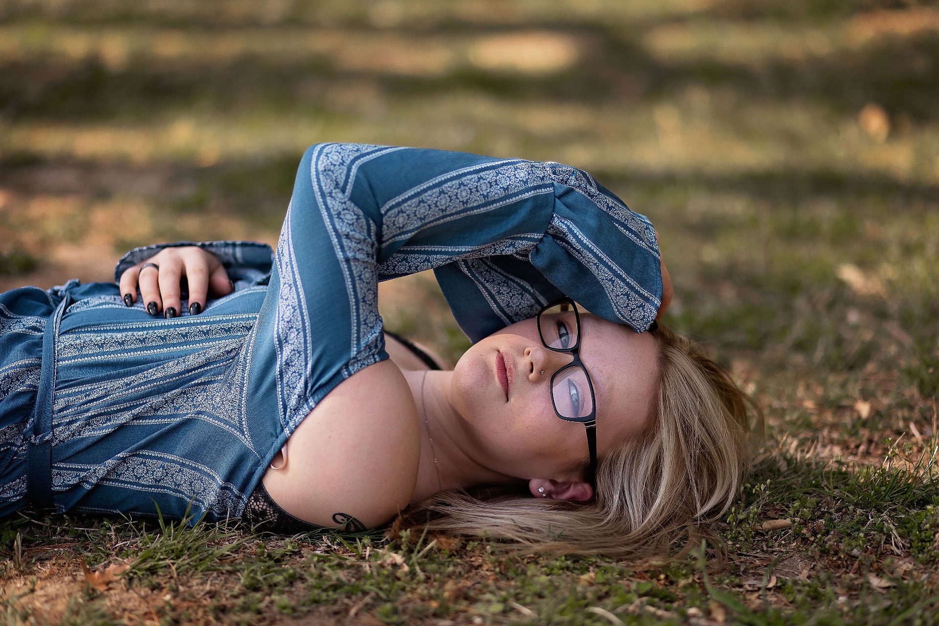 Senior lying on pine needles in a blue patterned dress, forearm resting over her forehead