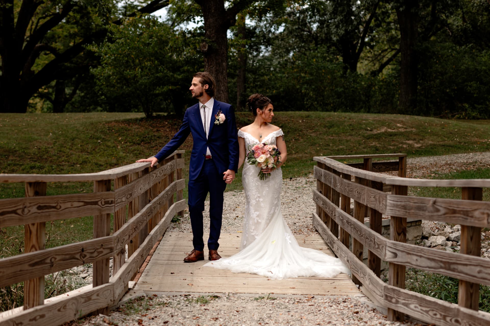Bride and groom standing on a wooden footbridge, each looking away from the other